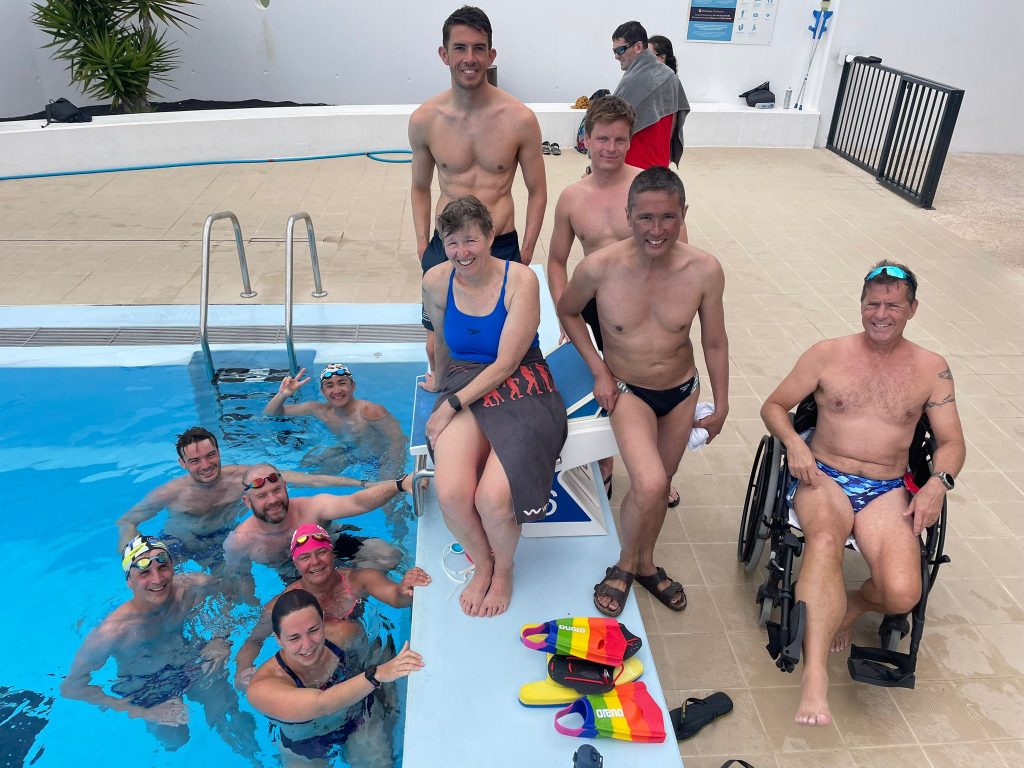 Queen of Hideous Swims #7 Michelle sits on a diving block surrounded by successful finishers of the Hideous birthday IM swim challenge